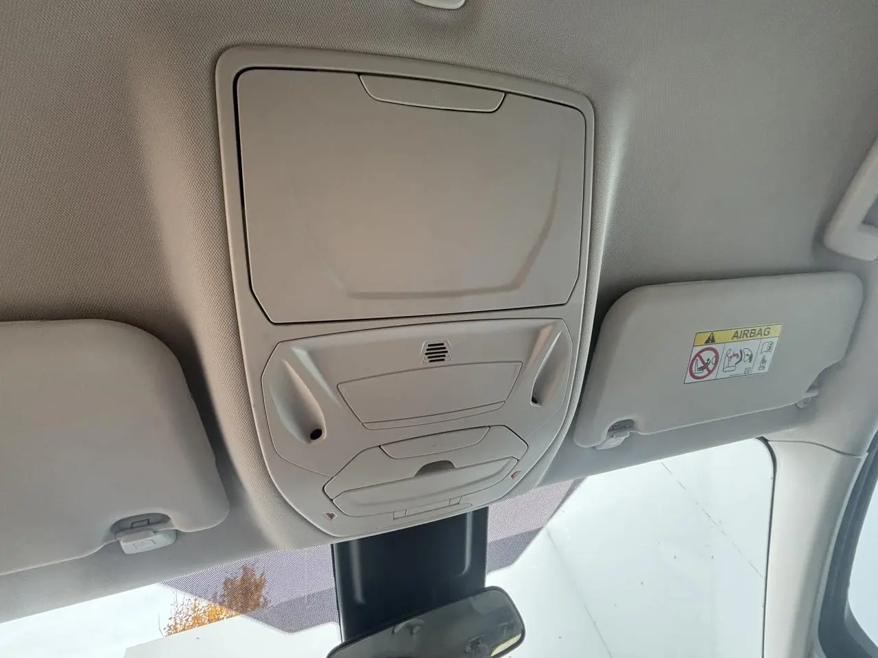 Vue intérieure du plafond avant d'une Ford C-MAX gris clair, montrant les commandes d'éclairage et les pare-soleil.