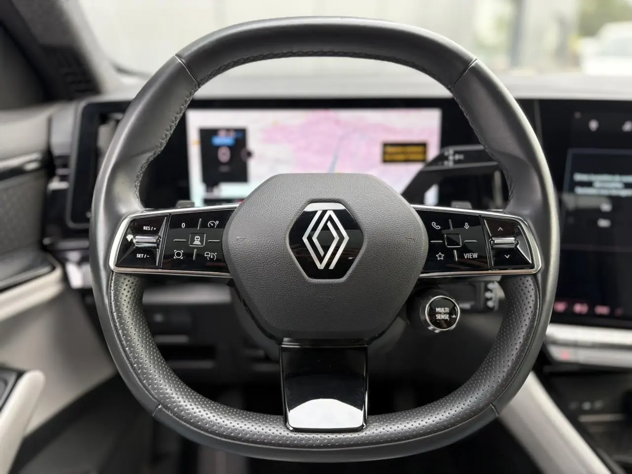 Volant cuir noir perforé de Renault Espace VI 6 E-Tech avec commandes intégrées et logo central, vue frontale intérieure.