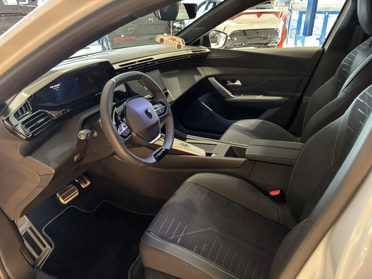 Intérieur avant droit de Peugeot 308 blanc Okenite 2026, volant compact GT cuir et tableau de bord numérique.