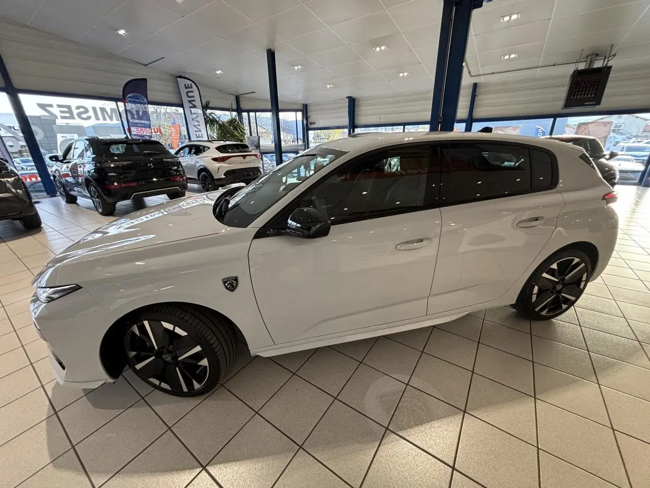 Vue latérale droite d'une Peugeot 308 blanche Okenite avec jantes alliage bi-tons et rétroviseurs noirs brillants en showroom.