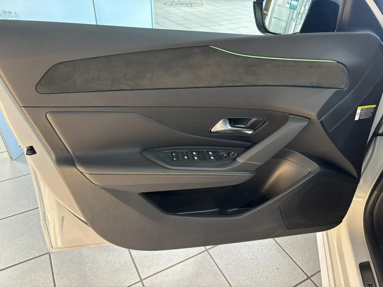 Vue côté gauche de la porte avant noire avec surpiqûres vert Adamite et insert Alcantara du Peugeot 308 Hybrid 2026 blanc Okenite.