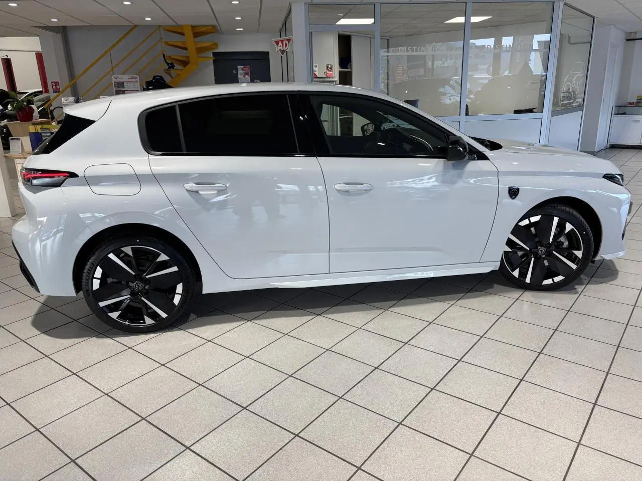 Profil droit d'une Peugeot 308 blanche Okenite avec jantes alliage 18" bi-tons et vitres surteintées en showroom.