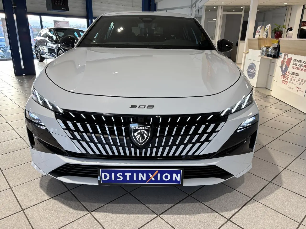 Vue de face d'une Peugeot 308 blanche Okenite avec calandre noire à motifs verticaux et logo lion lumineux.