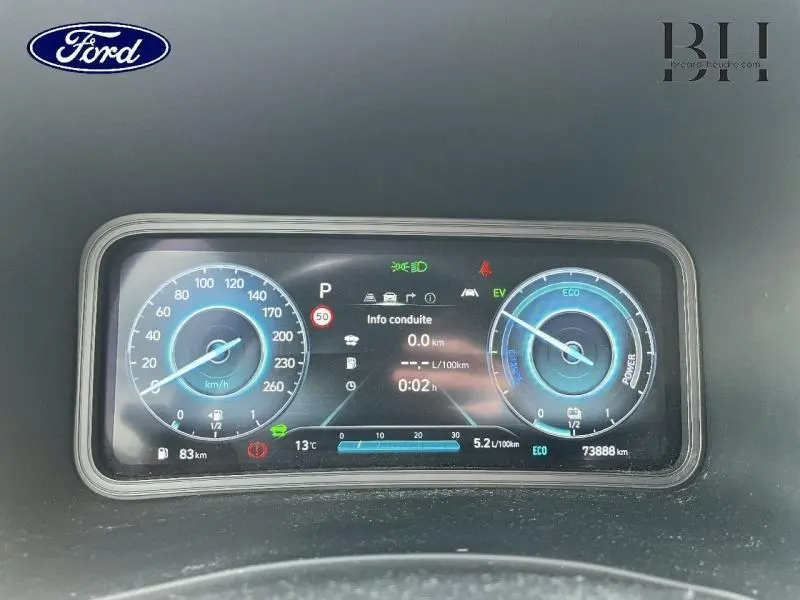 Tableau de bord numérique d'un Hyundai Kona hybride, affichage vitesse et consommation, vue frontale rapprochée.