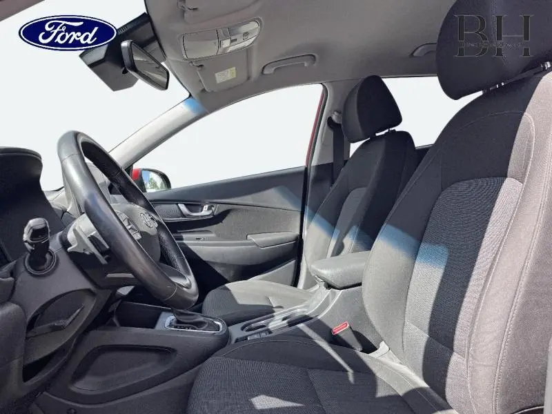 Vue intérieure côté conducteur du Hyundai Kona rouge, montrant les sièges noirs et le volant multifonction en cuir.