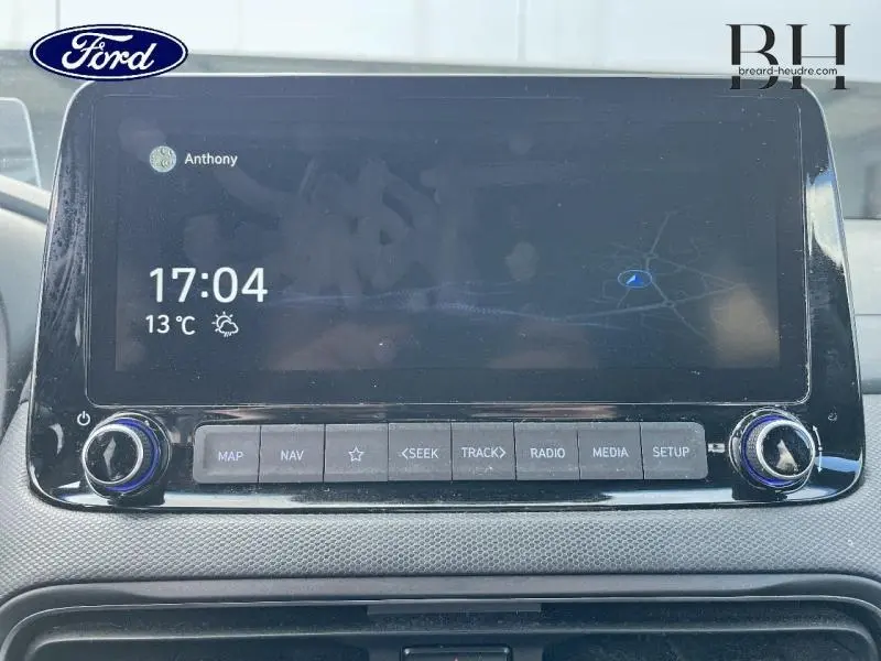 Écran tactile central de bord Ford affichant l'heure, la température et un GPS, avec boutons de commande en dessous.