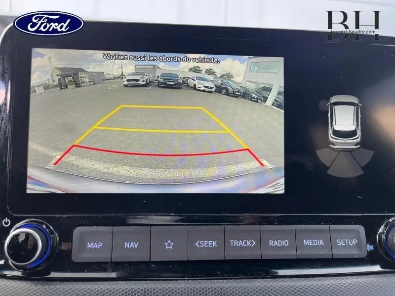 Écran de caméra de recul montrant l'arrière du Hyundai Kona rouge Pulse Metal avec lignes de guidage colorées.