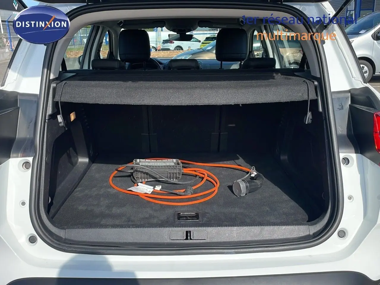 Coffre ouvert d'un Citroën C5 Aircross blanc nacré, montrant un câble de recharge orange pour hybride plug-in.