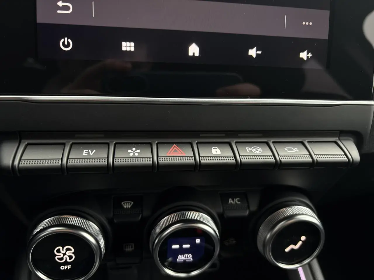 Gros plan sur la rangée de boutons de commande et les réglages de climatisation de la Renault Clio 2025 hybride noire.