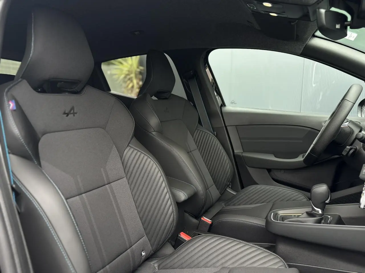 Intérieur de la Renault Clio Esprit Alpine 2025, vue côté gauche sur sièges sport noirs avec surpiqûres bleues.