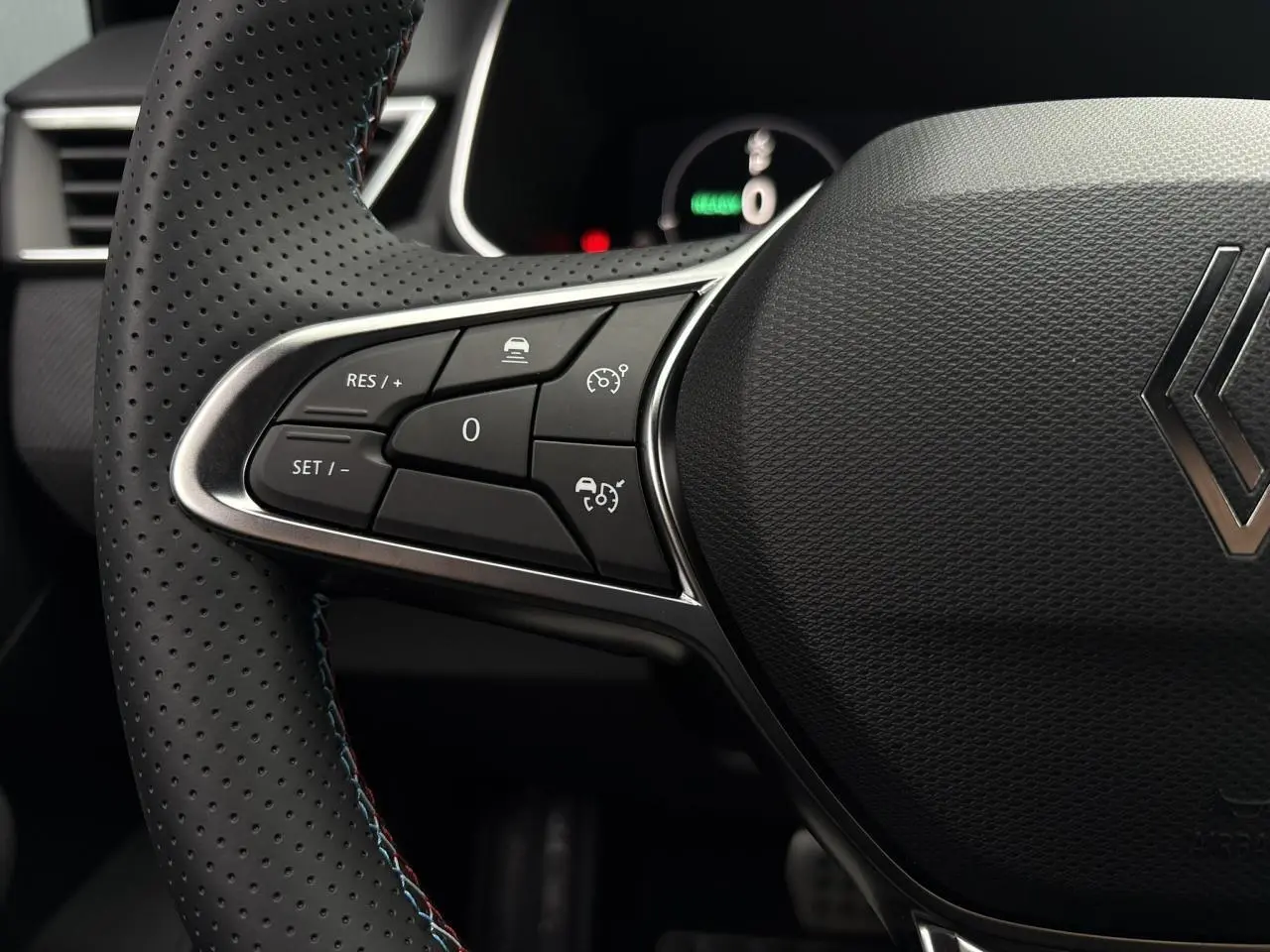 Gros plan sur le volant perforé noir avec surpiqûres bleues de la Renault Clio V NV E-Tech 2025, boutons multifonctions visibles.