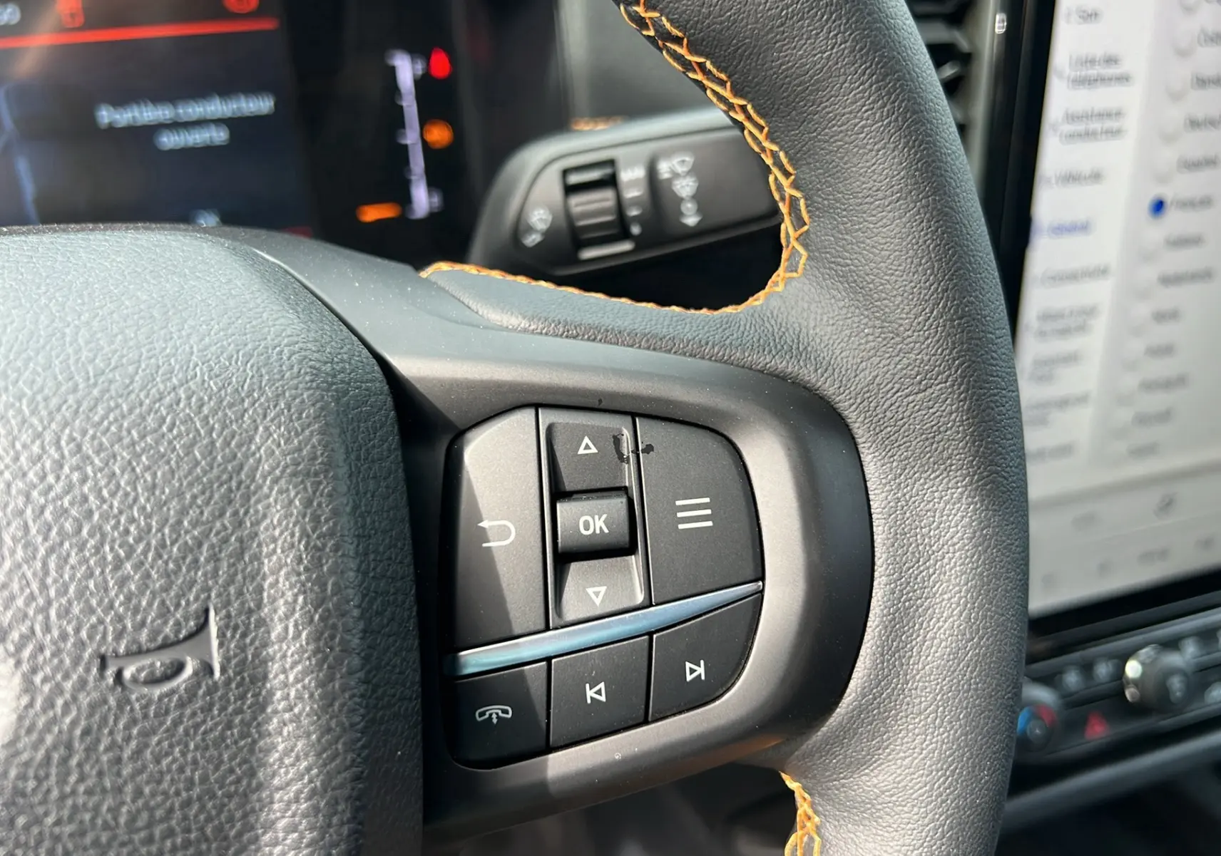 Gros plan sur les commandes multifonctions à droite du volant cuir noir avec surpiqûres orange du Ford Ranger blanc glacier 2025.