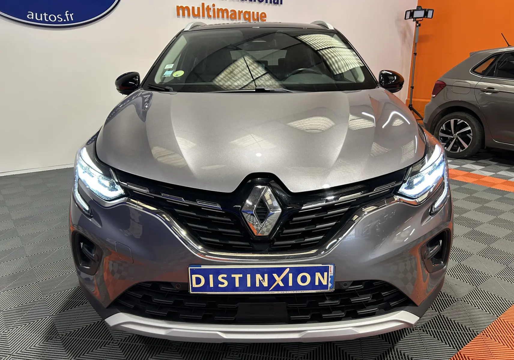 Vue avant d'un Renault Captur gris avec phares allumés et logo distinctif sur calandre noire brillante.