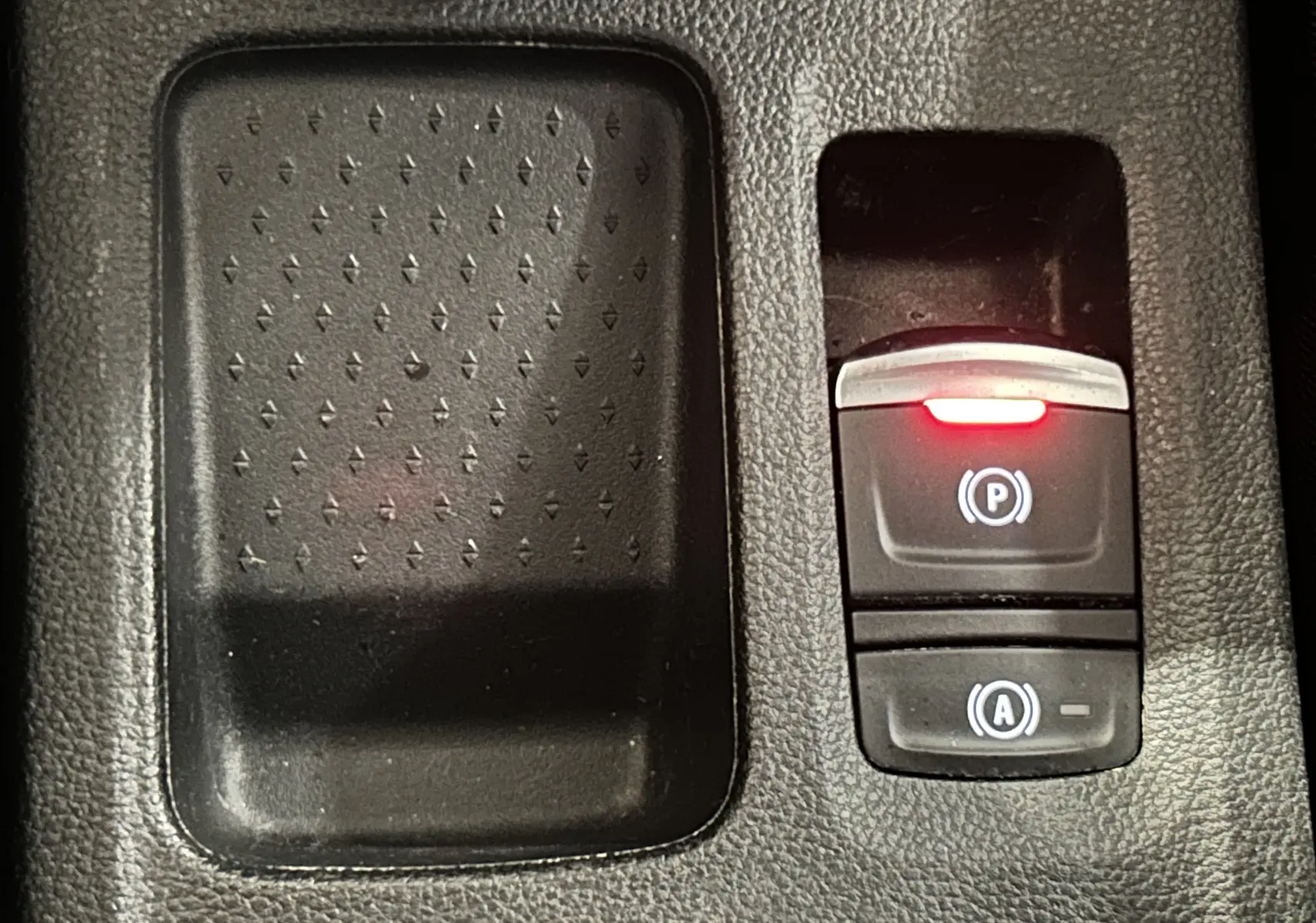 Gros plan sur la console centrale noire du Renault Captur 2020, avec bouton de frein à main électronique allumé en rouge.