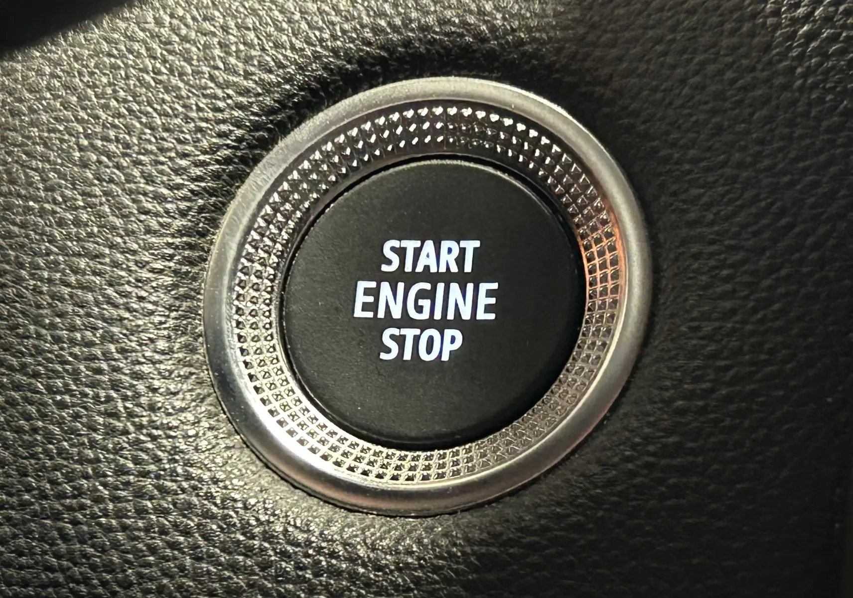 Gros plan sur le bouton Start Engine Stop entouré d'une bague métallique texturée dans l'habitacle noir du Renault Captur gris.