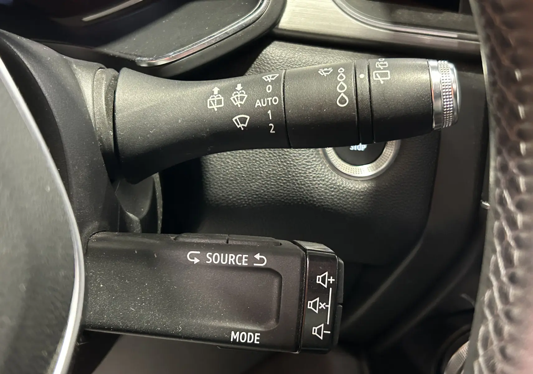Gros plan sur les commandes de volant noir du Renault Captur gris, avec bouton start visible en arrière-plan.
