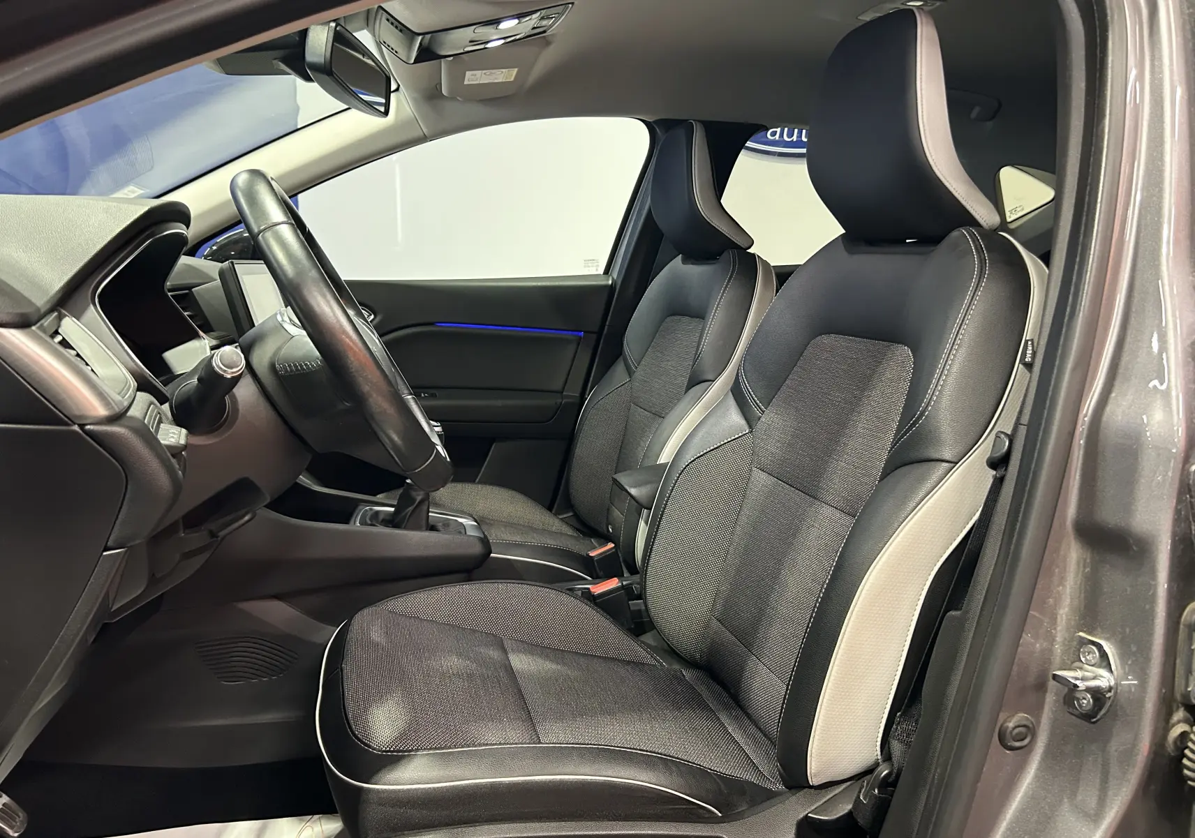 Vue intérieure côté conducteur du Renault Captur gris 2020, sièges bi-matière noirs et gris avec surpiqûres blanches.