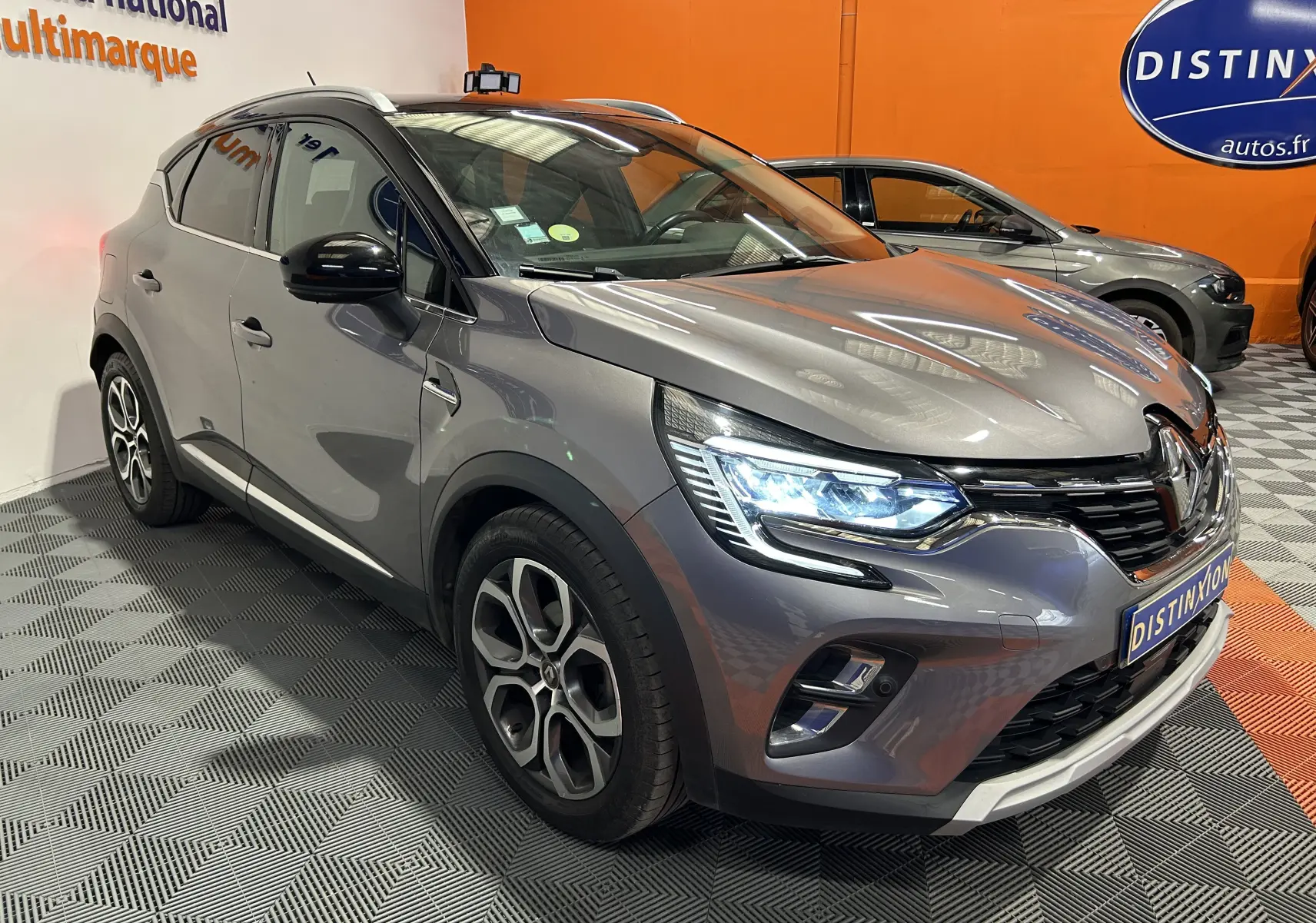 Renault Captur gris 3/4 avant droit avec phares LED allumés, jantes alliage et calandre noire brillante.