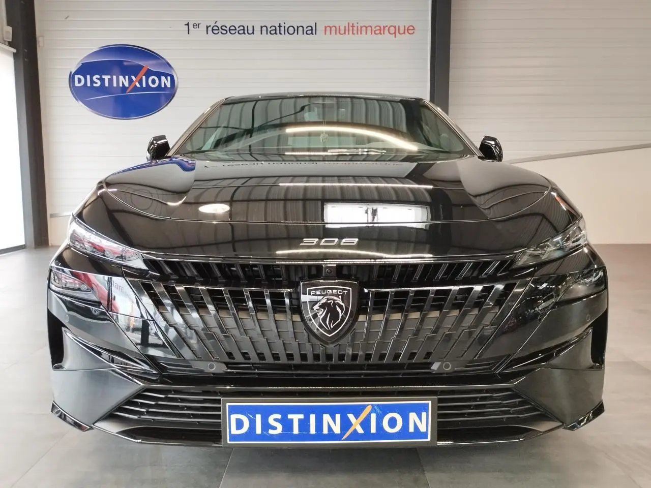 Vue frontale d'une Peugeot 308 noire métallisée avec calandre noire et logo lion central lumineux.