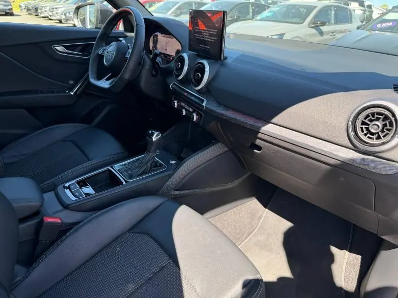 Vue intérieure côté conducteur de l'Audi Q2 35 TDI S line 2025, avec tableau de bord noir et écran central relevé.