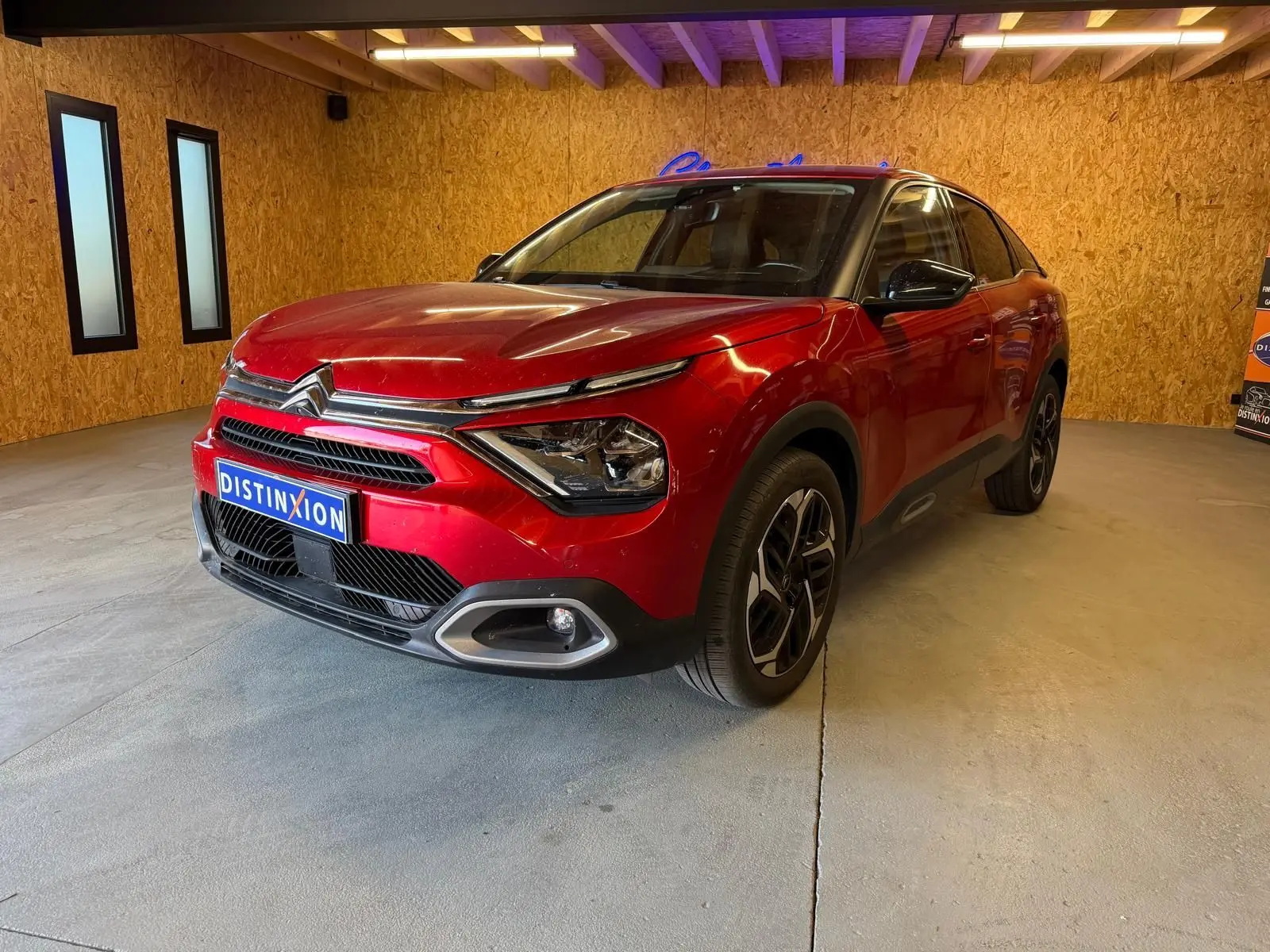 Citroën C4 X rouge vue 3/4 avant droit dans un garage avec éclairage intérieur et jantes noires.