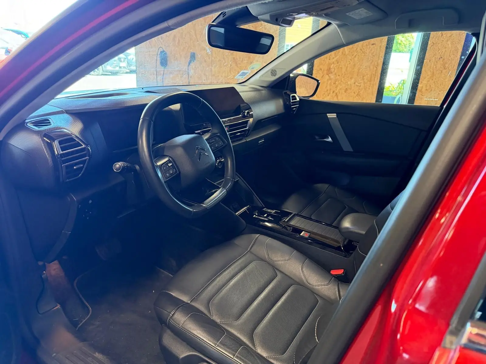 Vue intérieure côté conducteur de la Citroën C4 X rouge, avec sièges en cuir noir et tableau de bord moderne.
