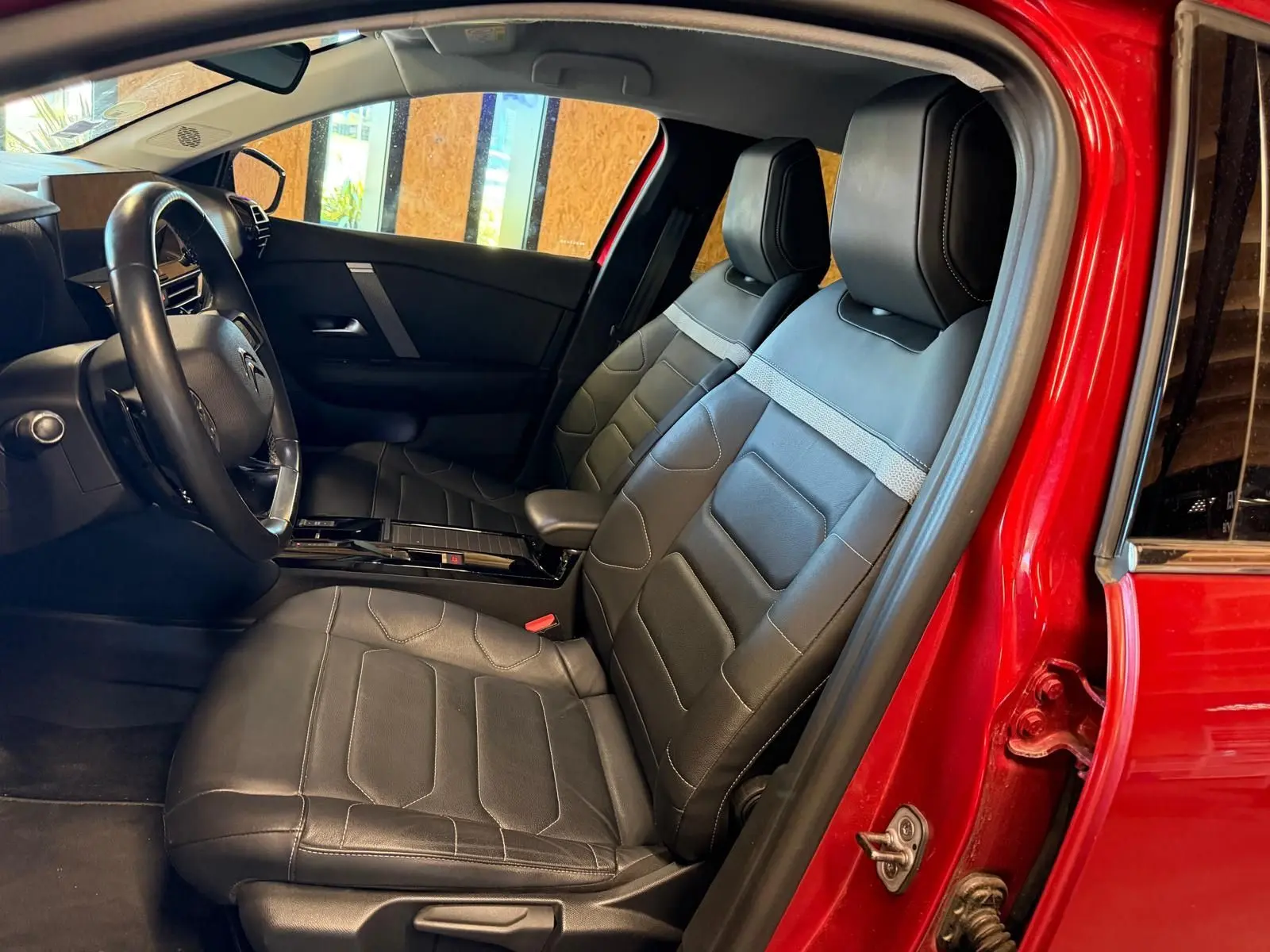 Vue intérieure côté conducteur de la Citroën C4 X rouge 2021, sièges avant en cuir noir avec surpiqûres grises.