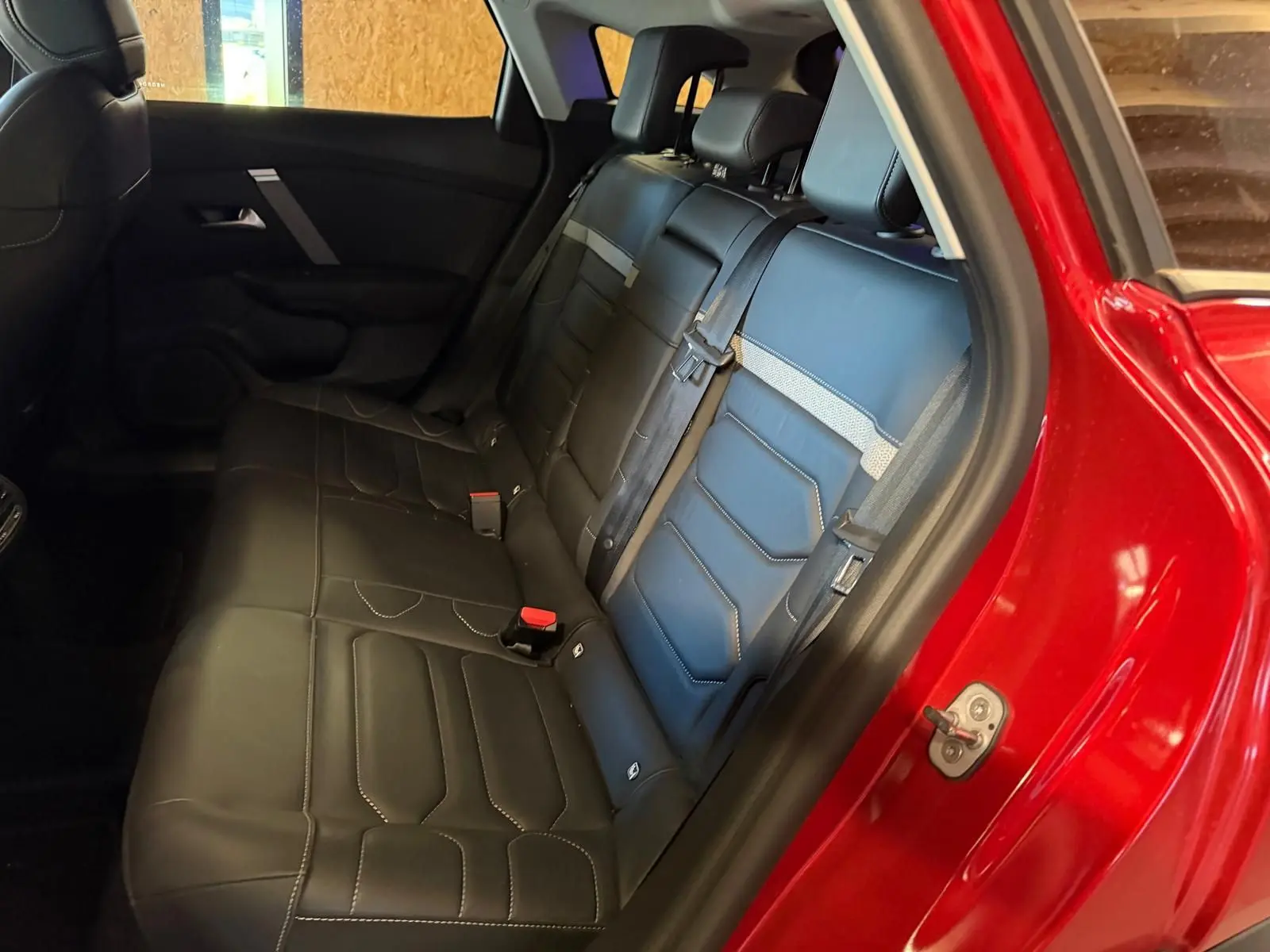 Vue intérieure côté gauche des sièges arrière en cuir noir de la Citroën C4 X rouge, avec ceinture de sécurité attachée.