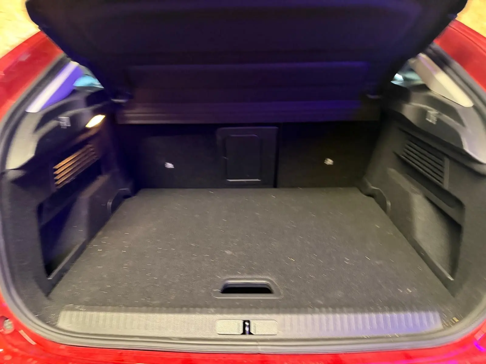 Coffre ouvert vu de l'arrière d'une Citroën C4 X rouge, montrant un espace de chargement noir et bien agencé.