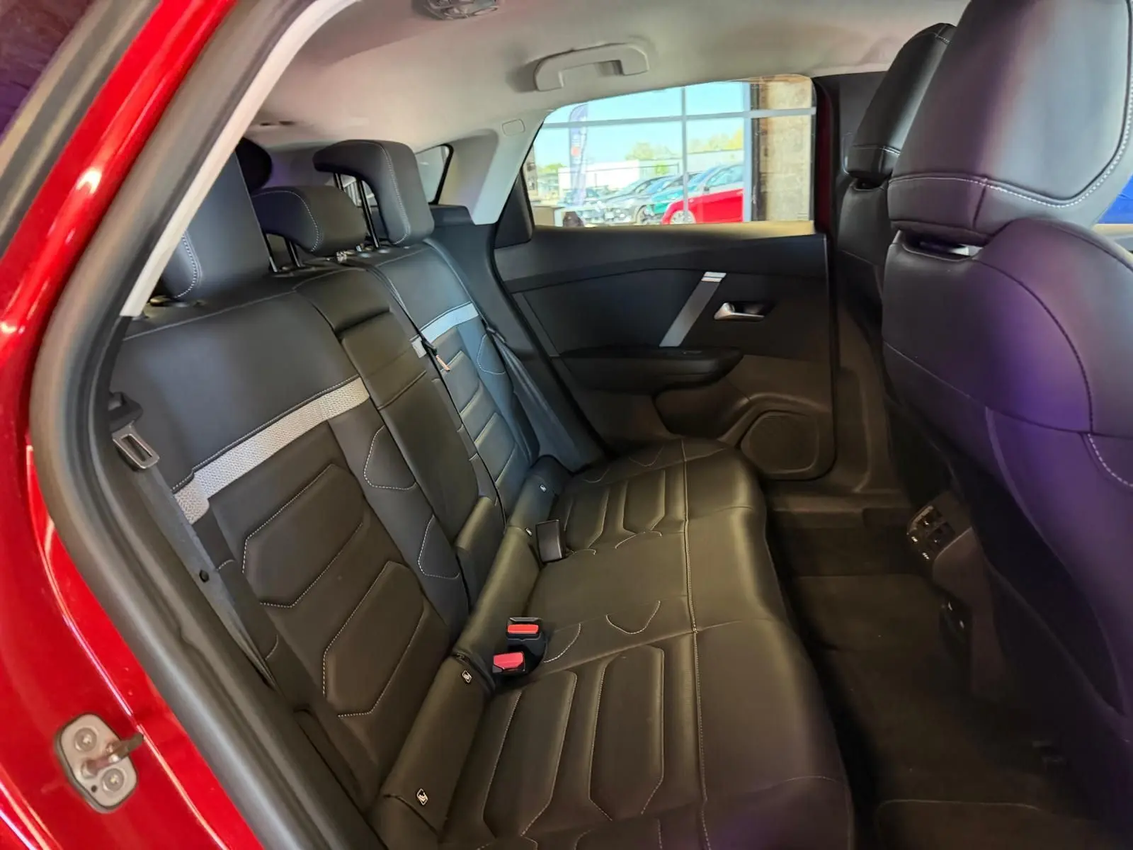 Vue intérieure côté arrière gauche montrant les sièges arrière en cuir noir avec surpiqûres blanches d'une Citroën C4 X rouge.