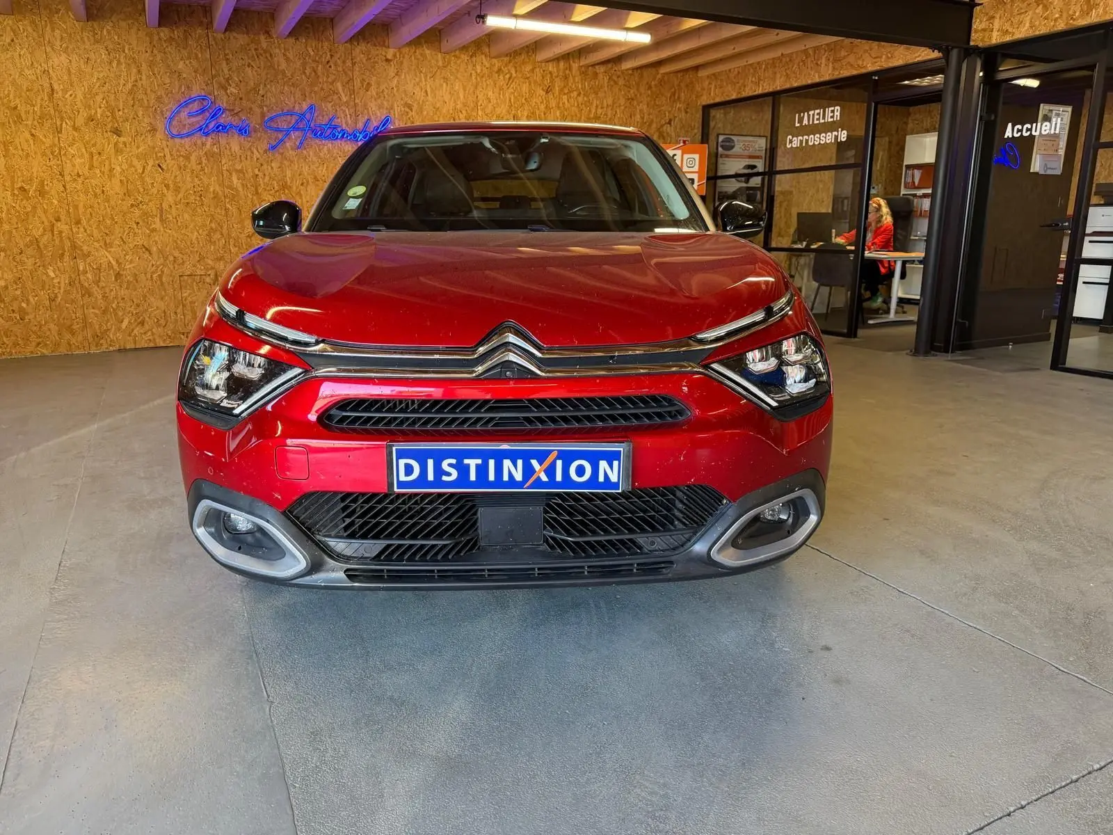 Vue de face d'une Citroën C4 X rouge 2021, avec calandre chromée et plaque Distinxion, en intérieur showroom.
