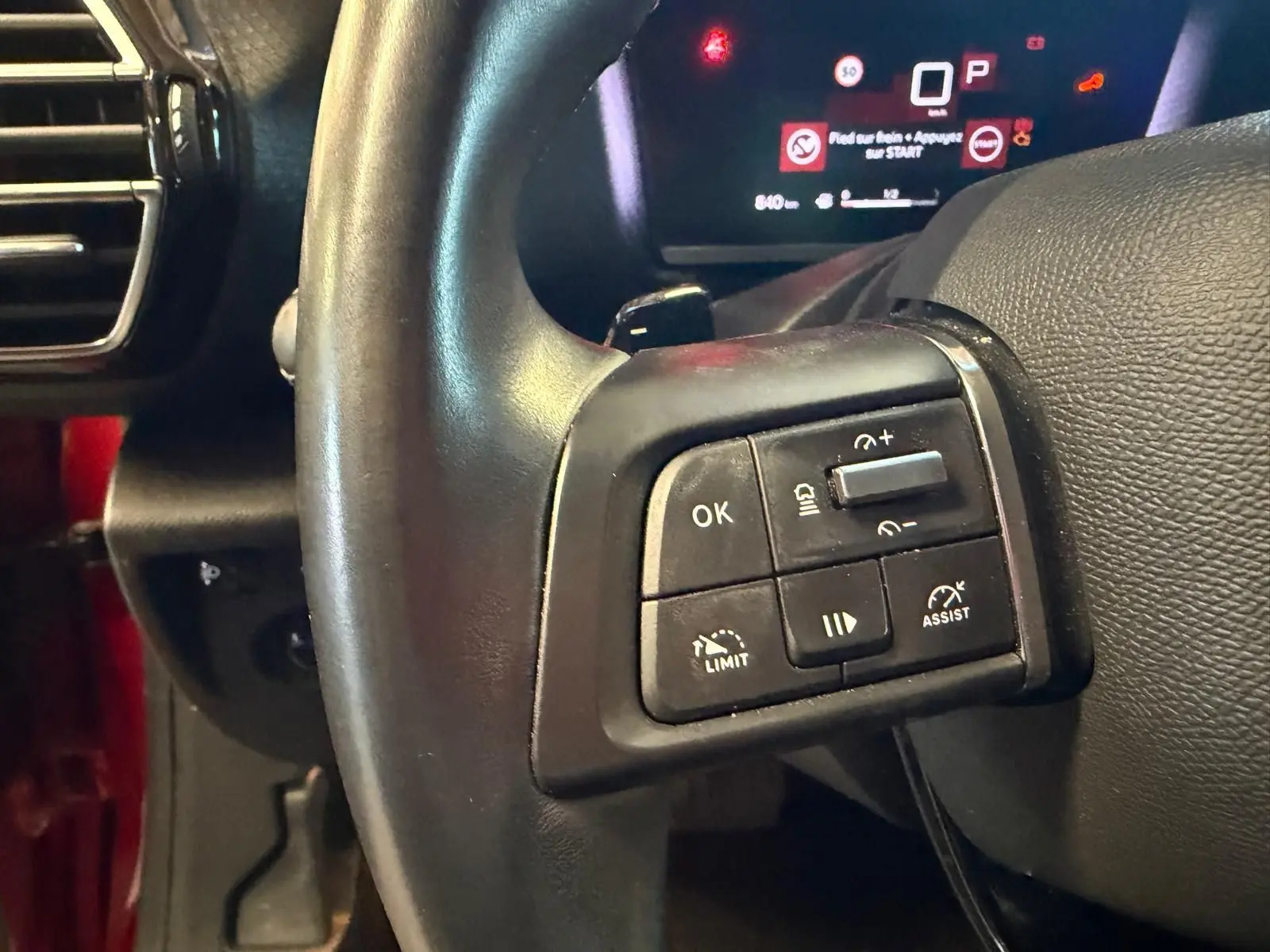 Gros plan sur les commandes au volant côté gauche d’une Citroën C4 X 1.5 BlueHDi 130 diesel, tableau de bord numérique en arrière-plan.