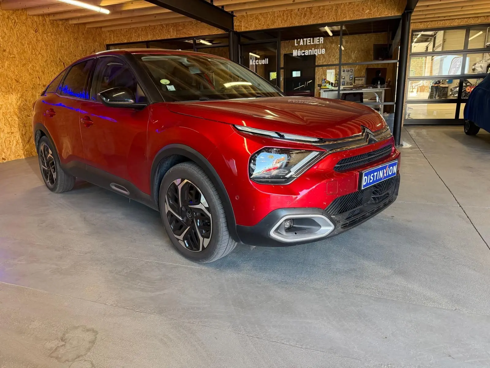 Vue 3/4 avant droite d'une Citroën C4 X rouge métallisé stationnée dans un garage avec détails noirs contrastants.