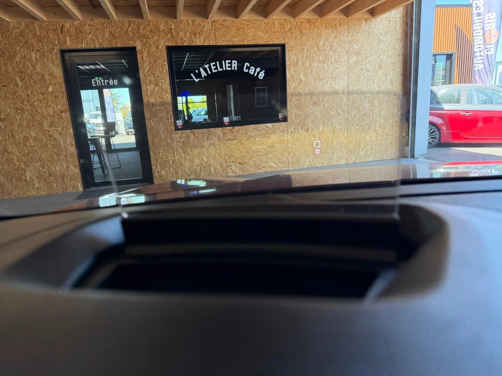Vue depuis l'intérieur du Citroën C4 X 2021, montrant le tableau de bord et le pare-brise face à un mur en bois clair.