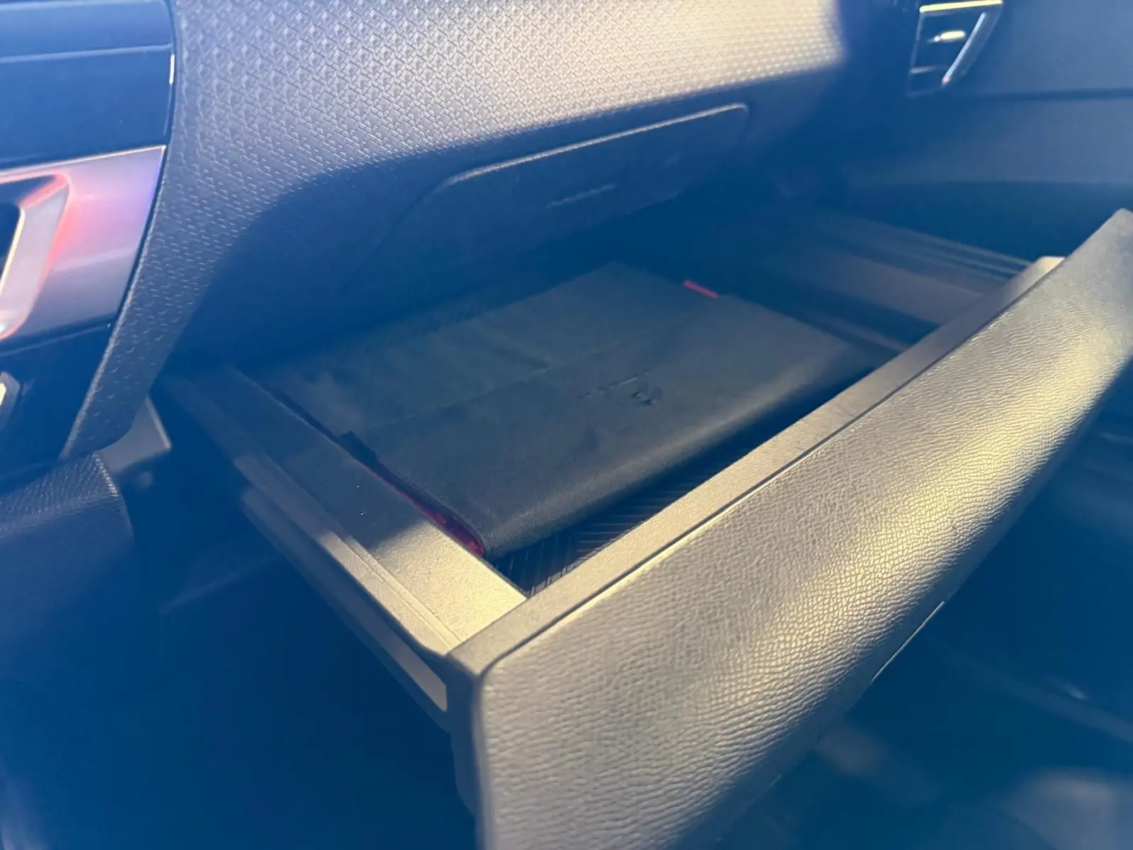 Gros plan sur la boîte à gants ouverte de la Citroën C4 X 1.5 BlueHDi 130, intérieur noir en tissu.