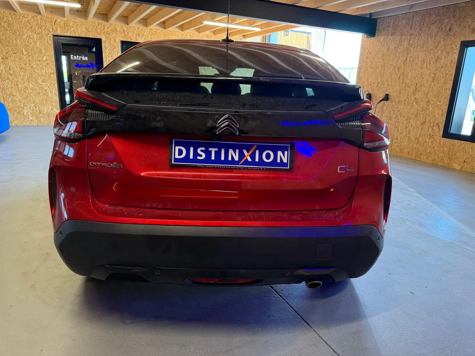 Vue arrière d'une Citroën C4 X rouge avec toit noir, dans un garage aux murs en bois clair.