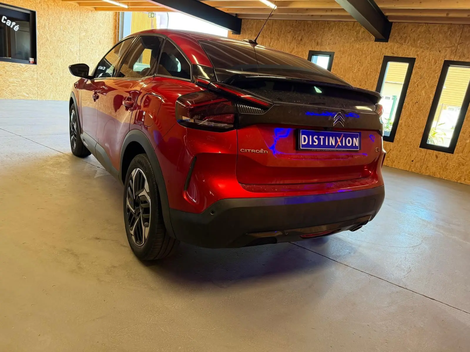 Vue 3/4 arrière droite d'une Citroën C4 X rouge métallisé avec toit noir dans un garage lumineux.