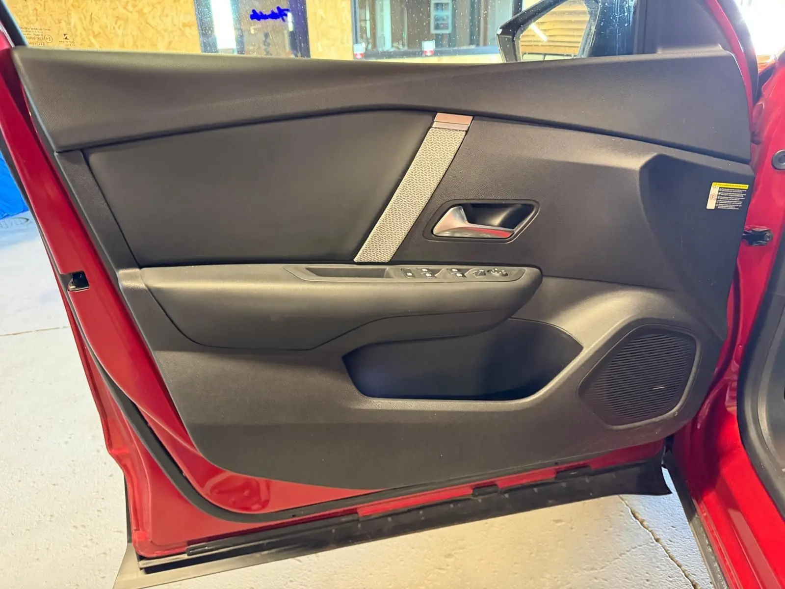 Vue intérieure de la porte avant gauche rouge d'une Citroën C4 X 2021 avec garniture noire et commandes de vitres.