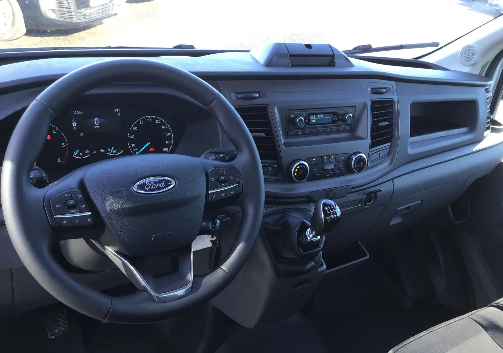 Vue intérieure du tableau de bord et volant du Ford Transit Châssis Cabine blanc, avec levier de vitesses manuel et commandes au volant.