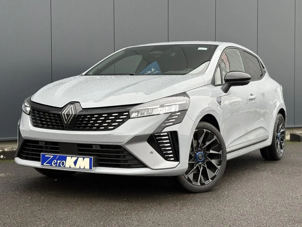 Renault Clio Gris Rafale vue 3/4 avant droit, avec calandre noire et jantes alliage noires distinctives.