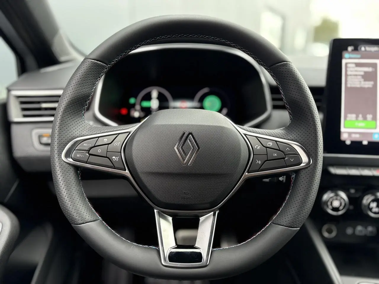 Volant en cuir noir perforé avec surpiqûres bleues de la Renault Clio E-Tech Gris Rafale, tableau de bord et écran tactile visibles.