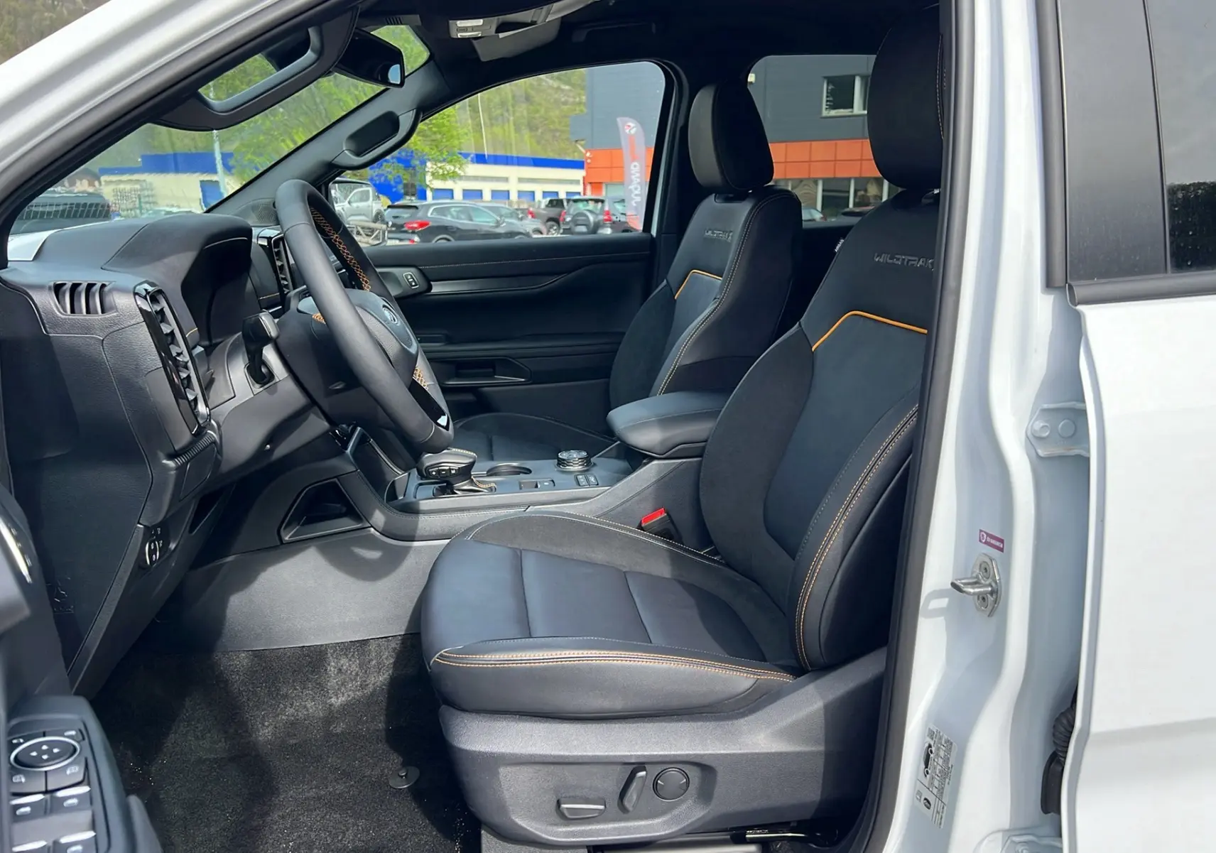 Vue intérieure côté conducteur du Ford Ranger blanc glacier 2025, sièges Wildtrak noirs avec surpiqûres orange et volant cuir.