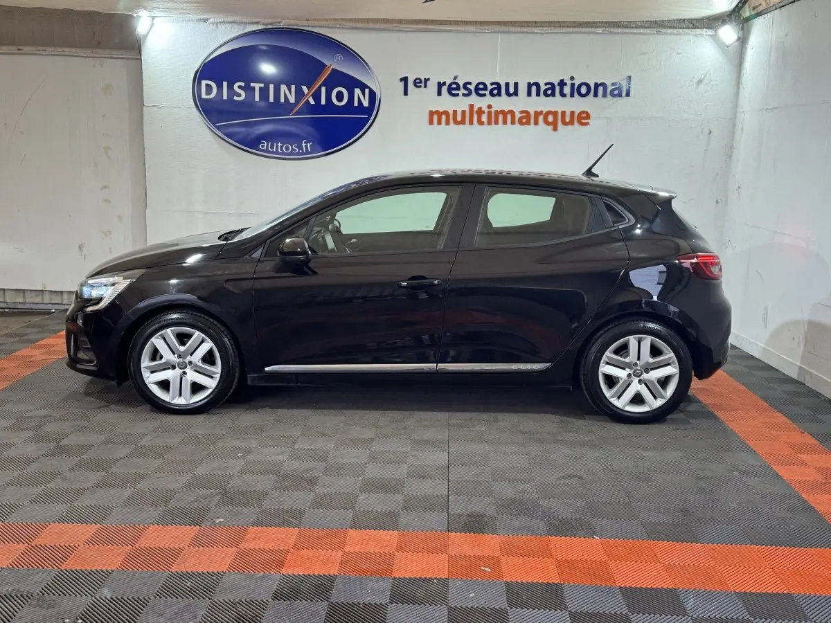 Profil droit d'une Renault Clio Business E-Tech hybride 140 noire, stationnée en intérieur avec jantes argentées et logo Distinxion en arrière-plan.