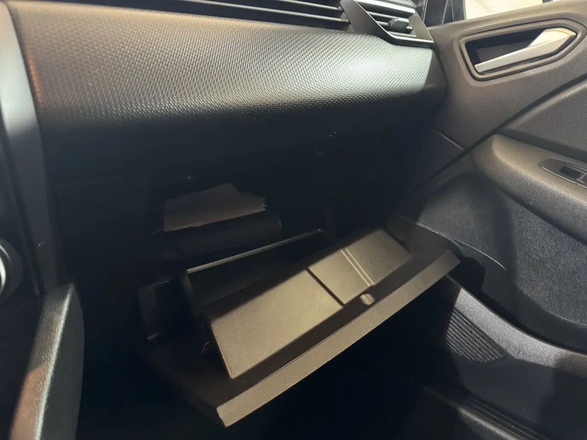 Vue intérieure côté passager de la boîte à gants ouverte sur tableau de bord noir texturé d'une Renault Clio Business E-Tech hybride.