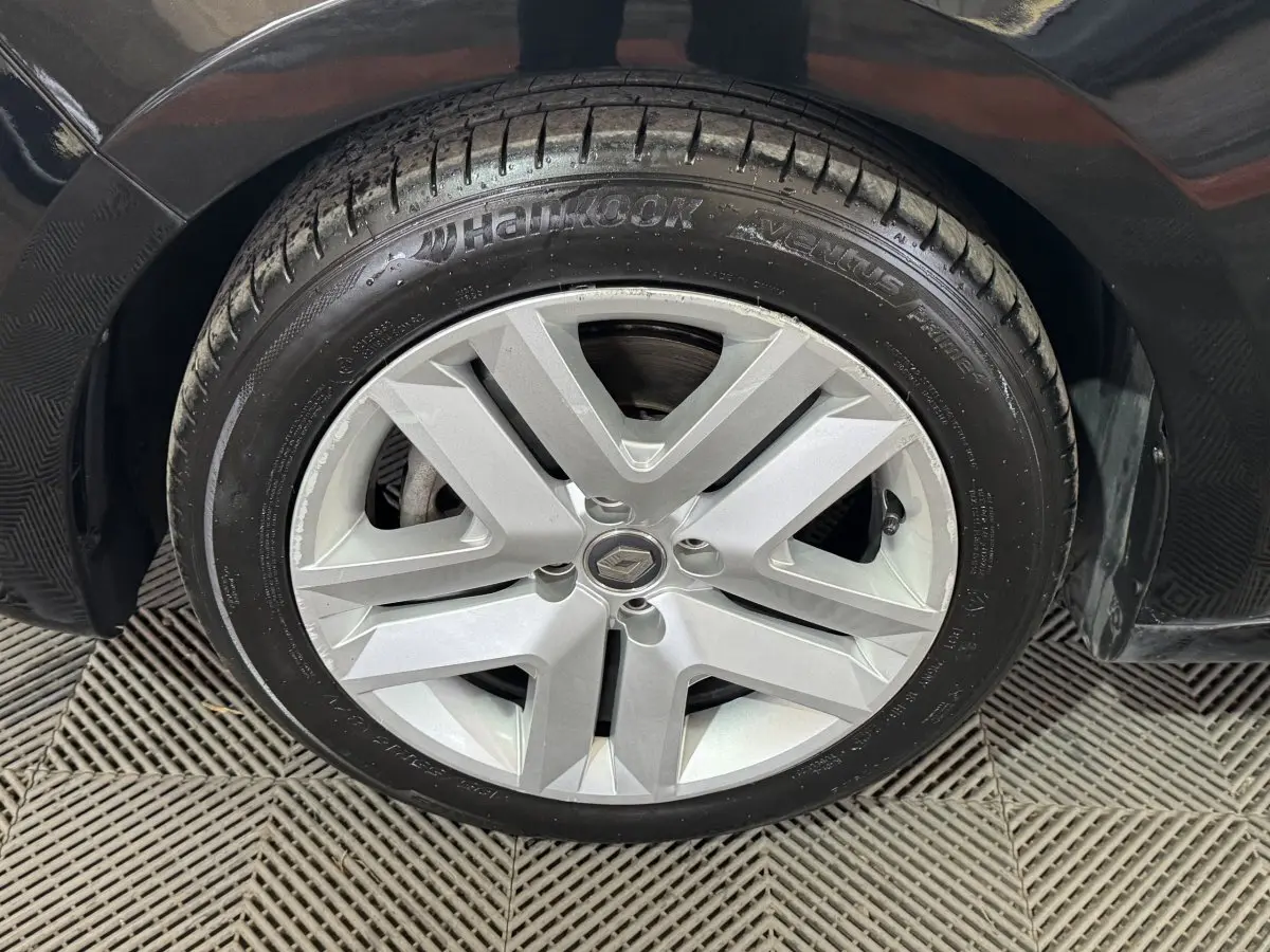 Gros plan sur la roue avant droite noire d’une Renault Clio Business E-Tech hybride 2021 avec jante argentée à cinq branches.