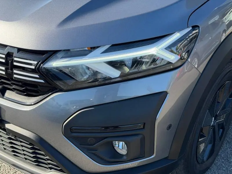 Gros plan sur le phare avant droit du Dacia Jogger 2025 gris Schiste métallisé avec détails LED et partie de la calandre noire.