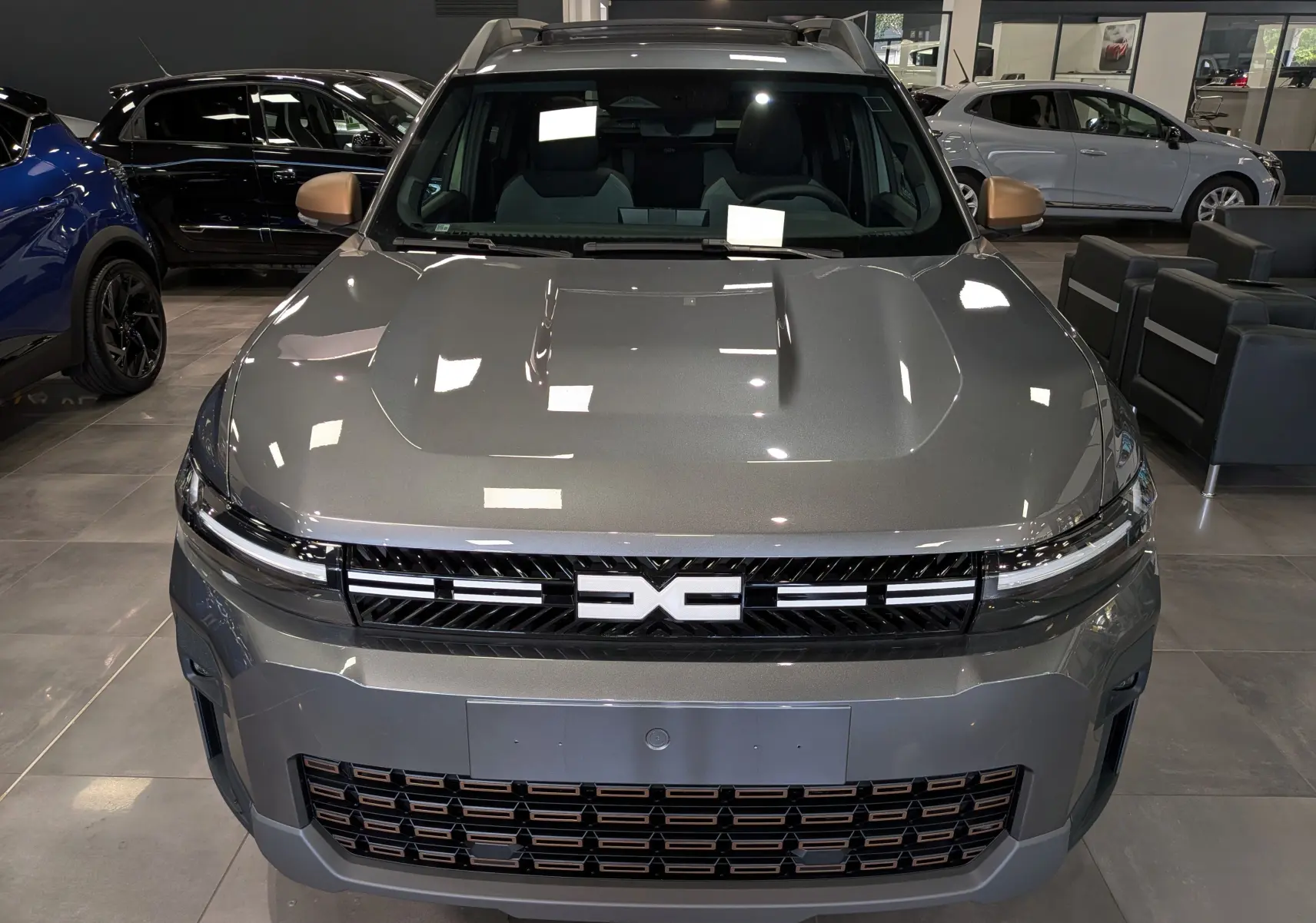 Vue frontale du Dacia Bigster Hybrid-G 150 4x4 gris schiste avec calandre noire et détails cuivrés en showroom.