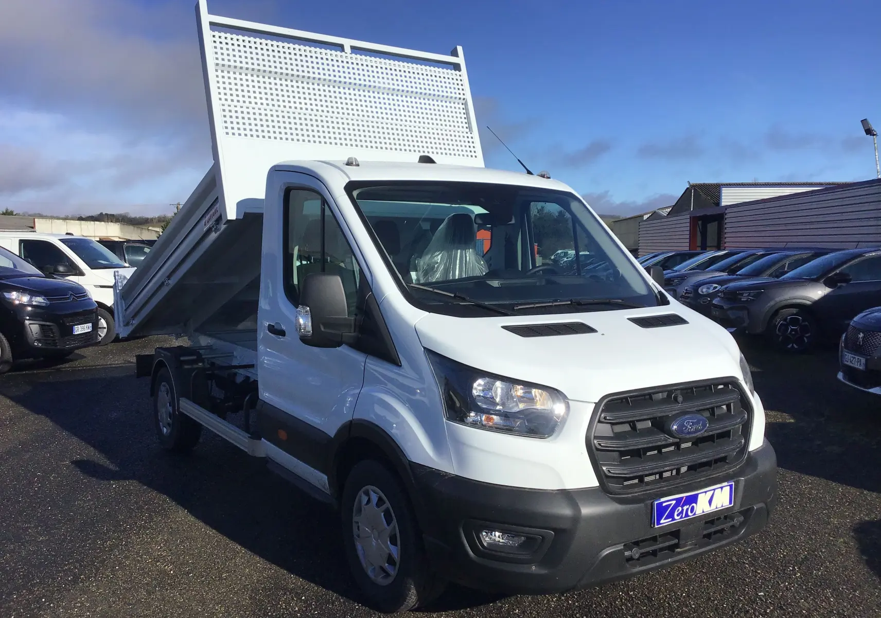 Ford Transit Chassis Cabine blanc en 3/4 avant droit avec benne relevée sur parking extérieur.