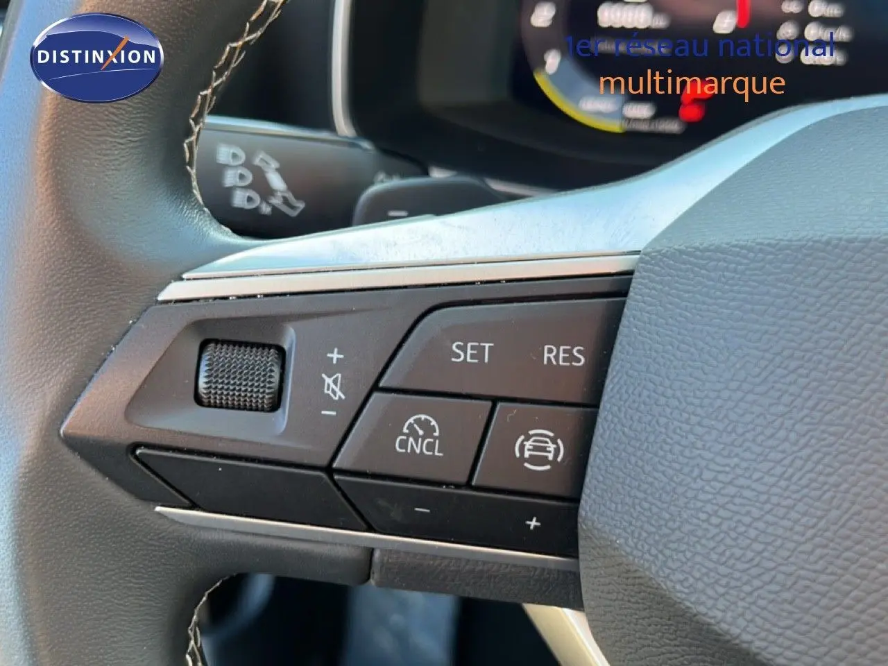 Gros plan sur les commandes au volant à gauche d'une SEAT LEON gris magnétique 2025, avec régulateur de vitesse et volume.