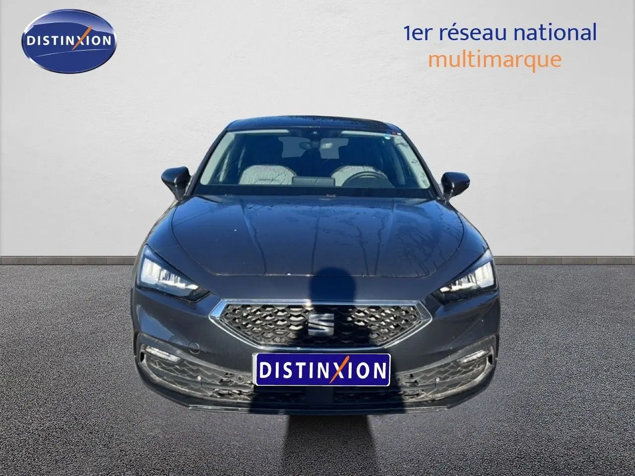 Vue frontale d'une SEAT Leon gris magnétique métal 2025 avec calandre hexagonale et phares LED allumés.